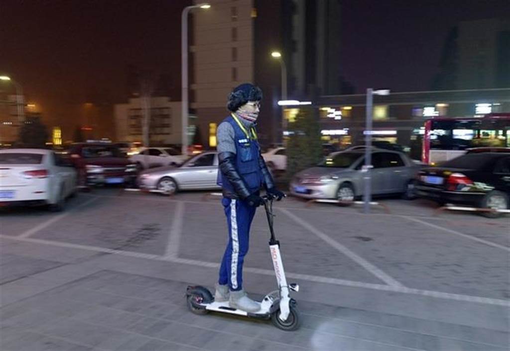 12月22日，余桥骑着电动滑板车穿行在城市街道旁，寻找需要代驾的顾客。（新华社）