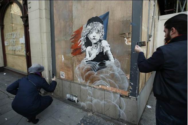行人拍攝Banksy在法國大使館附近畫的塗鴉。(美聯社)