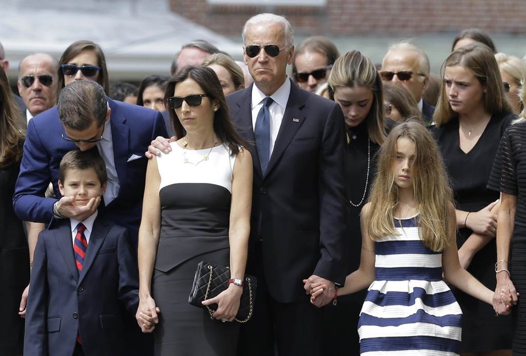 拜登一家于2015年6月6日出席波伊的葬礼，韩特（左）低头亲吻丧父的侄子杭特（Hunter）。而拜登则拥着媳妇海莉（左三），并牵着波伊的女儿娜塔莉（Natalie），强忍白髮人送黑髮人的悲痛。（图/美联社）