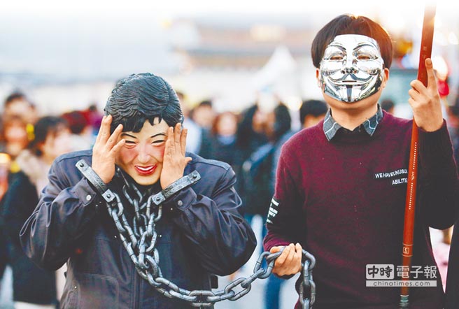 V怪客上陣！在南韓首爾市中心11日的反朴槿惠遊行活動中，1名民眾戴著朴的面具，手上繫著手銬與鎖鍊，另名戴著「V怪客」面具的民眾則牽著鎖鍊，象徵朴槿惠遭到司法制裁。（路透）