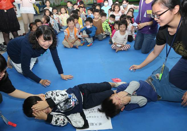 小朋友地上滚滚滚，体验遇到身上着火千万不要跑，要先用双手保护脸部、躺在地上左右滚动，压熄火点。（黄国峰摄）