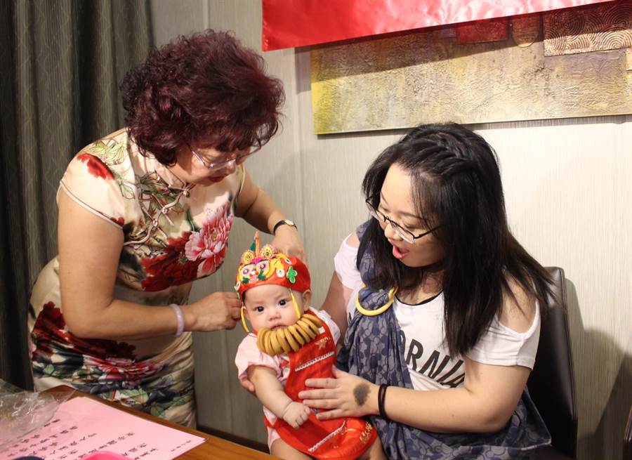老師謝美雲（左）幫寶寶掛上收涎餅乾，萌樣融化了在場的許多長輩。（圖/陳淑娥）