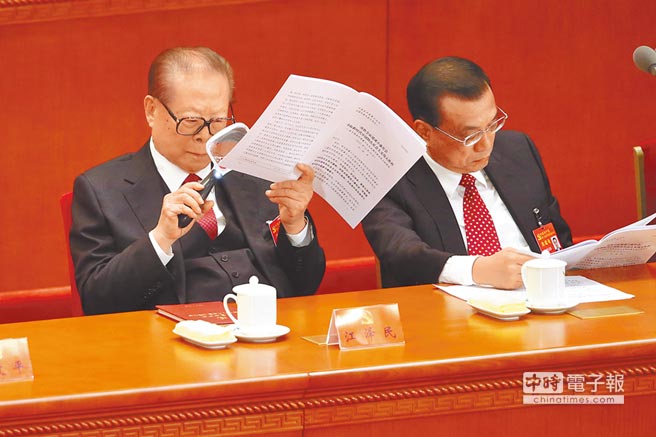 中共前總書記江澤民(左)拿放大鏡仔細看著手中的工作報告。（中央社）