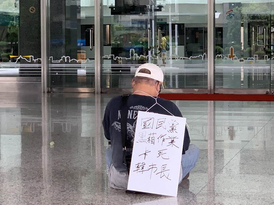 有一男子戴著口罩與帽子，在高雄市政府靜坐，身上的牌子寫著「國民黨黑箱作業卡死韓市長」、「絕食請求韓市長選總統」。(柯宗緯攝)