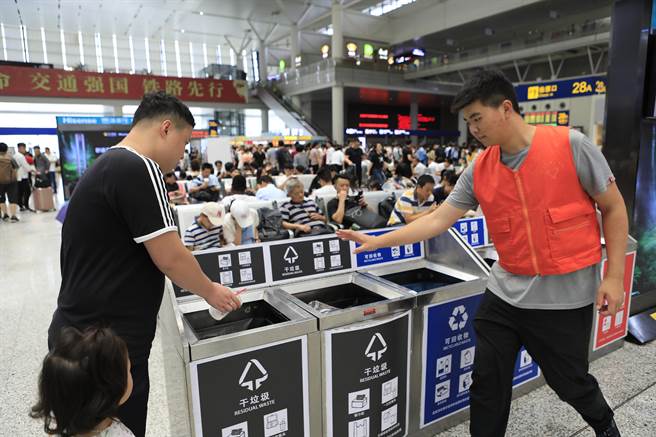 被稱為史上最嚴垃圾分類措施的《上海市生活垃圾管理條例》7月1日正式實施。圖為鐵路上海虹橋站志工幫助旅客對垃圾進行分類。（圖／中新社）