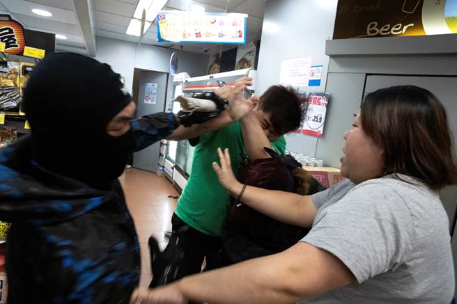 穿着绿色上衣的香港市民遭到着黑衣的示威者围殴，满脸是血躲入商店求救，一名妇女试图阻止他们继续行使暴力。（图／路透）