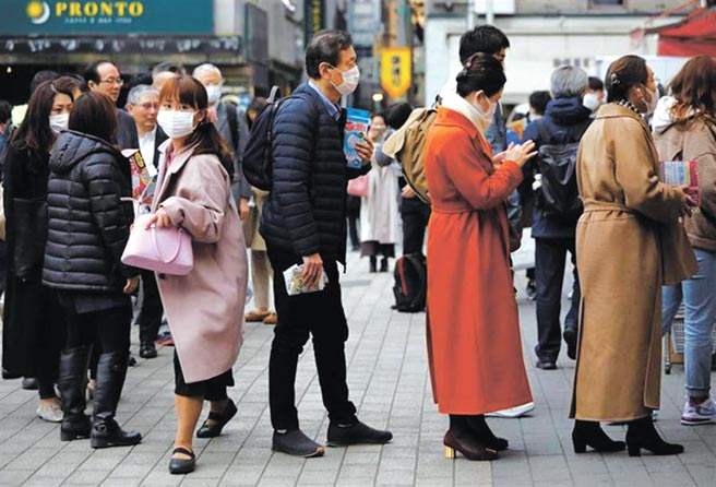 日本新冠肺炎疫情升級，東京民眾14日爭相到藥局排隊買口罩。（路透）