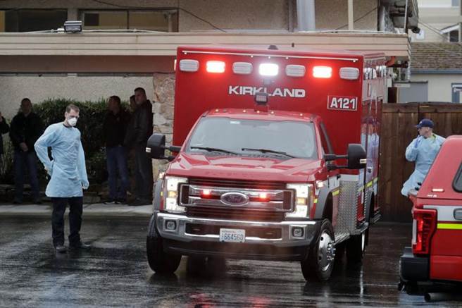 美国华盛顿州「柯克兰长照中心」（Life Care Center of Kirkland）不断传出确诊与死亡病例，图为工作人员6日站在救护车旁的画面。（美联社）