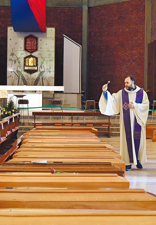 义大利北部塞里亚泰一座天主堂内，一名神父向成排的灵柩洒圣水，随后这些棺木就被军车运往坟场埋葬。（路透）