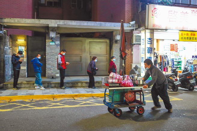 新冠肺炎疫情，令厂商看坏未来景气。图为下班时段民眾依序排队，前往药局买口罩，一位摊商，推着摊车，正准备回家。（邓博仁摄）
