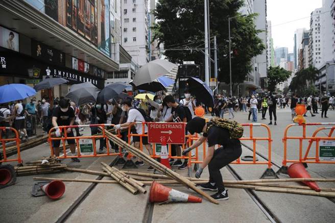香港反國安法遊行，抗議群聚拆除交通設施堵住道路與警方對峙，以雨傘防衛警方催淚彈。（圖／路透）
