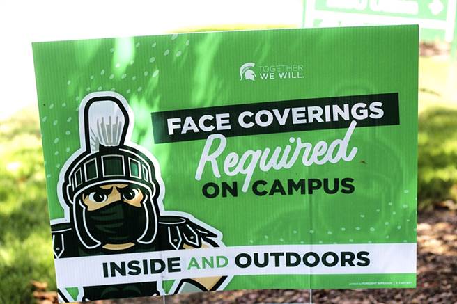 早前美國密西根州立大學學生到處開趴、聚會，導致3周內確診人數激增將近15倍。圖為設立在校園內、呼籲學生戴口罩的告示牌。（圖／美聯社）