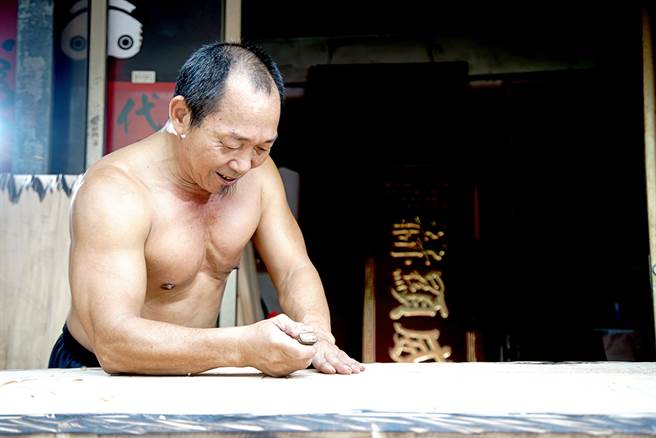 打赤膊製作匾額的吳崑章，是鳳山佛具街「三民路」生活裡的一道日常風景。（圖/曾信耀攝）
