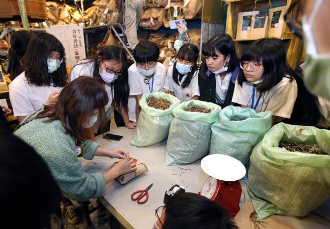 姚德和青草号老板娘正在教成渊高中学生如何包好药材。（赵双杰摄）