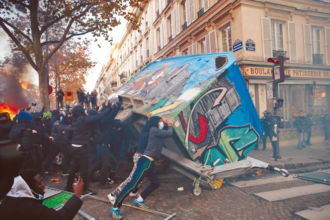 法國日前發生類似美國警察施暴非裔事件，政府推動整體安全法，引發全法國遊行示威。年輕人推倒放在路旁建築。（美聯社）