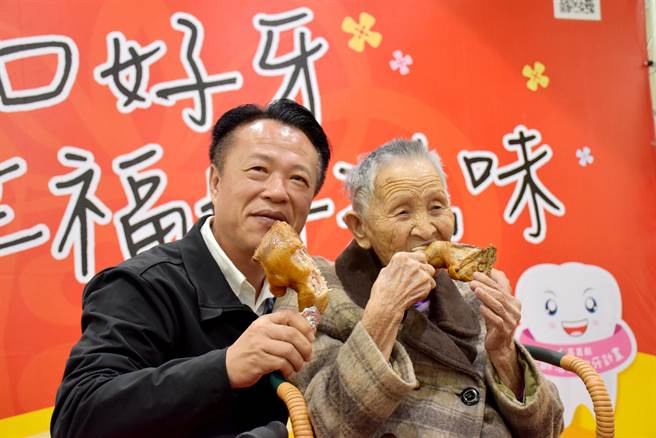 嘉义县长翁章梁（左）上任后推动「65岁以上长者及55岁以上原住民」乐龄活动假牙补助，至今逾万人完成装置，14日百岁人瑞陈阿嬷（右）大口啃鸡腿，展现装假牙成果。（吕妍庭摄）