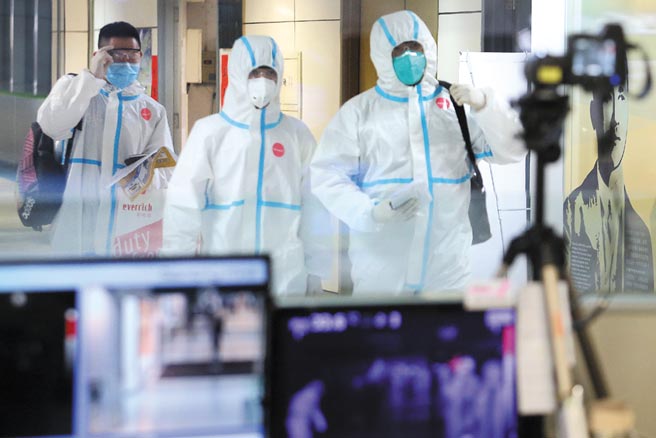 专家担忧若不及时採取强而有力的防疫手段，一旦变种病毒散播速度加快，感染人数大增，恐击溃当地医疗资源。图为桃园机场第二航厦入境管制区内，3名身穿防护衣的旅客，正通过发烧筛检站。（范扬光摄）