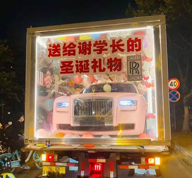 小货车上载着以透明胶框罩着的粉红色劳斯莱斯，引起路人驻足围观。框上贴着大号字体标语「祝23岁谢学长圣诞节快乐」。（图／微博）