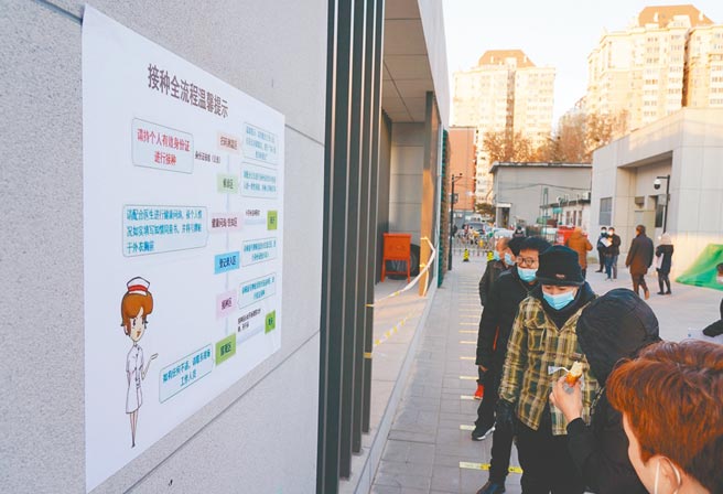 1月3日，北京民眾在接种点外排队接种疫苗时观看接种流程图。（新华社）