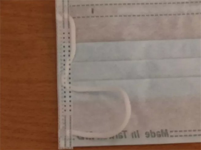 网友PO出被「封印」的口罩，从照片中可见，口罩左边的挂耳直接被压在边缘的内层，只剩下一半的绳子露在外面。(图/截自Dcard)