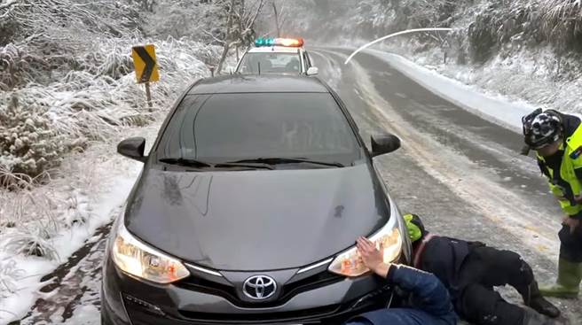 民眾车辆雪链掉链，员警倒卧结冰路面协助加挂。(宜兰三星分局提供)