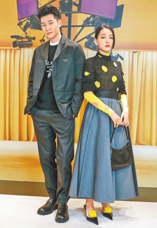 周兴哲（左）、林映唯共同现身Prada 2021春夏时装秀，周穿Re-Nylon单排扣西装外套7万6000元、经典标志圆领毛衣5万3000元、Re-Nylon西装长裤3万7500元、白色口袋衬衫2万7500元、抛光皮革德比鞋3万3500元；林映唯穿挖洞高领内搭4万2000元、挖洞高领毛衣3万3000元、伞状长裙13万元、Cleo手提肩背包6万2000元、三角标志别针单支耳环1万3500元、皮革拼色高跟鞋3万3500元。（粘耿豪摄）