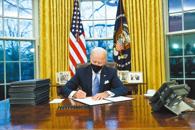 美国总统拜登20日就职后，当天即投入工作。图为拜登在白宫椭圆形办公室内签署行政命令。拜登的命令推翻川普政府多项政策，如重返世卫组织、终止兴建美墨边境围墙等。（路透）