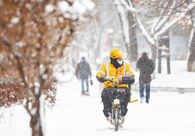 新疆烏魯木齊市日前迎來一場大雪，1名外送員頂著寒風在路上送餐。（新華社）