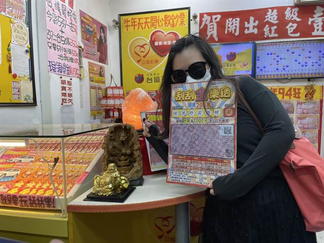刮中200万元头奖的幸运儿「芮姐」今天现身彩券行，拿出得奖刮刮乐彩券与店内吉祥物「倒流香龙」开心合照。（李俊淇摄）