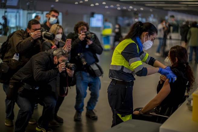 西班牙25日开始为优先人员接种疫苗，图中马德里一名警察正在接种阿斯利康疫苗，媒体抢着为她拍照。（图／美联社）