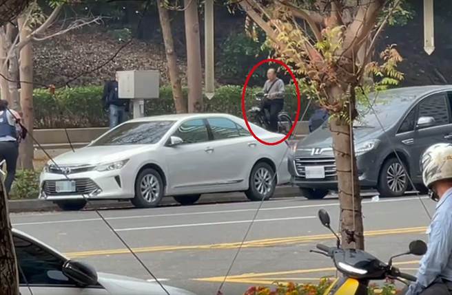 高雄市立美术馆豪宅区路边发生枪战，绑匪刚遭员警开19枪击毙，一名阿伯骑着单车「路过」现场，浑然不觉。（影片截图）
