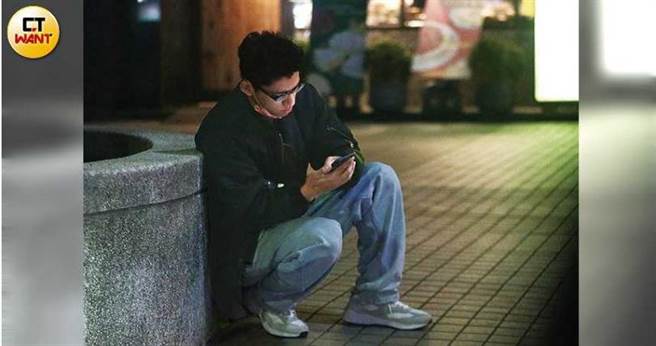 走出捷運站後，朱軒洋蹲在路邊滑手機等人。（圖／攝影組）