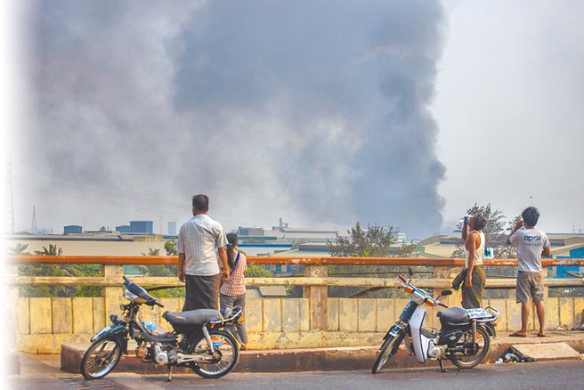 緬甸仰光驚傳外資工廠遭打砸搶燒，圖為民眾在遠處觀看遭到縱火的工廠飄出的濃煙。（美聯社）