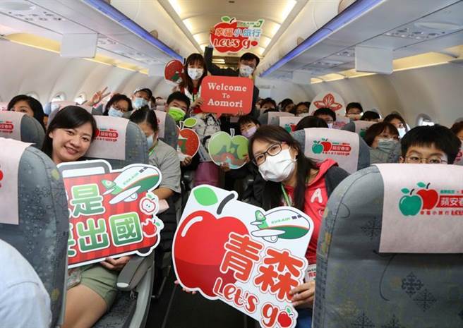 （长荣航空「苹安春来」青森类出国航班特别使用以青森苹果为主题设计的枕头套及头垫布布置机舱，并将登机音乐更换为「睡魔祭」的祭典音乐，营造宛如置身青森的氛围，旅客开心地拿着手拿牌合影留念。图／长荣航空提供）
