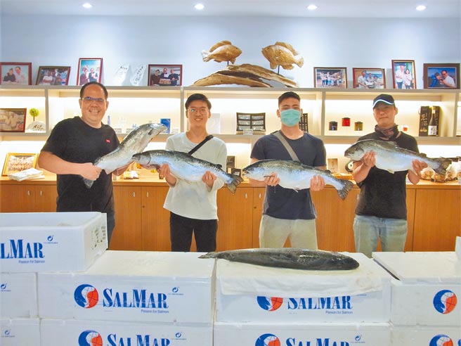 云林县口湖乡口湖渔类生产合作社送整尾大鲑鱼，首日有9名「鲑鱼人」抱得鲑鱼归，其中3人合照留念，由右至左分别为「杨亚太爱吃鲑鱼鲍鱼」、「周鲑鱼」、「杨鲑鱼」。（张朝欣摄）