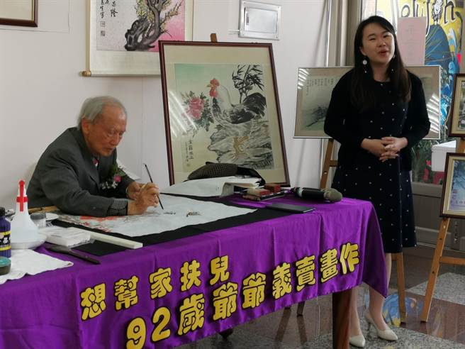 高齡92歲的畫家姚民生（左）現場揮毫義賣，孫女蔡言箴在旁獻唱爺爺愛聽的祝福歌曲。（劉秀芬攝）