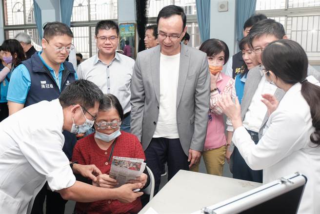 创立「银光未来创新协会」的朱立伦（中）了解验光师初步配老化眼镜的度数，请长辈看报纸能否看清字。（罗浚滨摄）