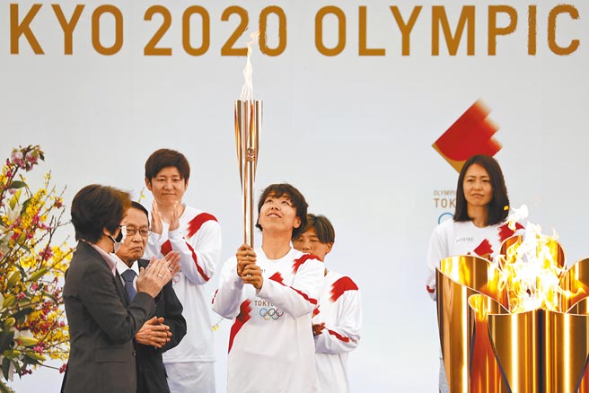 东京奥运圣火3月25日从日本福岛开始传递，由2011年勇夺世界杯冠军的日本女足队担任第一棒，手举圣火者为后卫岩清水梓，左一则是东京奥运筹委会主席桥本圣子。（美联社）