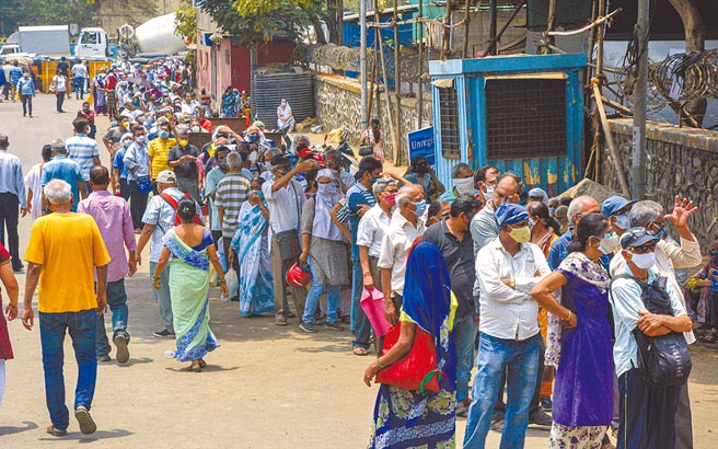 印度新冠疫情失控，26日大批民眾戴著口罩在孟買等待接種新冠疫苗。（新華社）