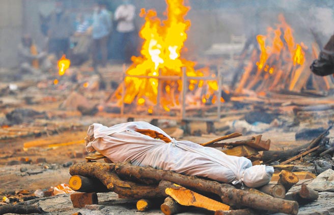 印度新冠疫情严峻，首都新德里1处火葬场，将染疫死亡的遗体放置在木柴堆上，一一火化。（路透）