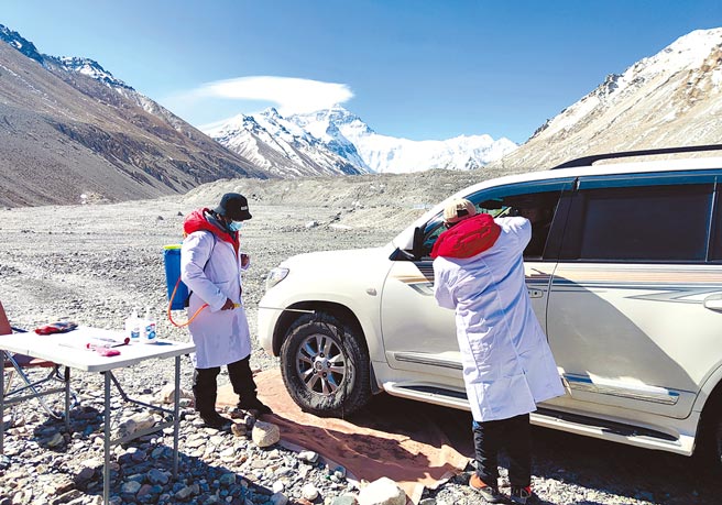 圖為大本營外防疫卡點的工作人員為進入營地的工作車輛消毒，並為駕駛員量體溫。（新華社）