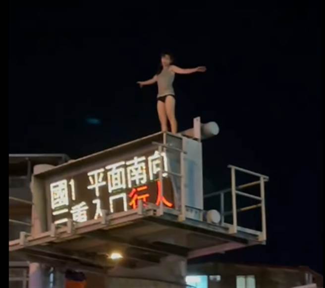 一名女子仅着背心、内裤爬上国1三重交流道旁8公尺高的电子告示牌。（照片来源：记者爆料网）
