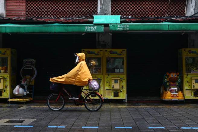 由于锋面笼罩台湾地区，台湾各地31日普遍降下滂沱大雨，台北市因疫情加上大雨，路上人车不多，一位妇人穿上雨衣做好防疫，骑车经过因疫情没有营业的场所。（邓博仁摄）
