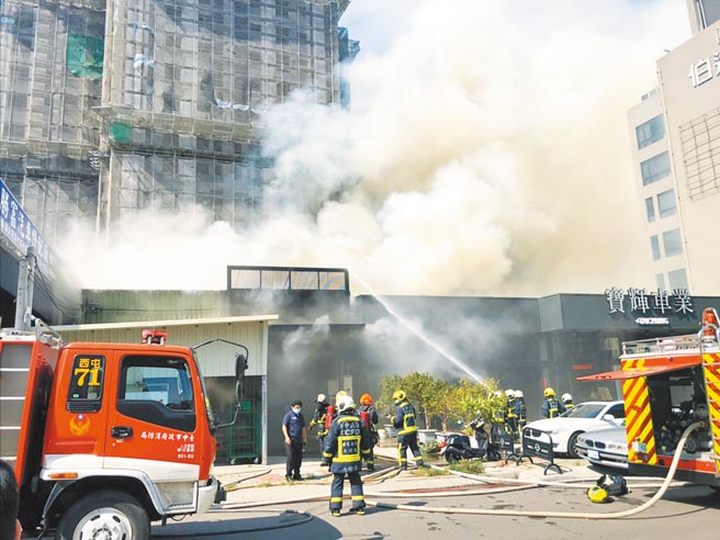 台中市西屯區福星西路一棟鐵皮屋，14日下午發生火警，鐵皮屋毗鄰的超跑車行險些被波及，消防人員利用水線防止火勢蔓延。（民眾提供／陳世宗台中傳真）