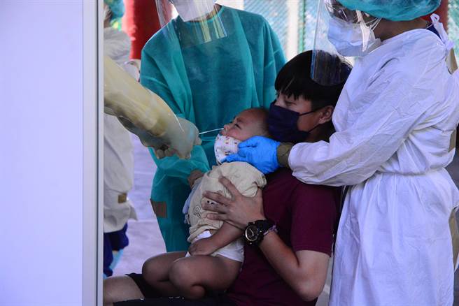 妈妈抱着小婴儿快筛，棉花棒插入鼻孔，嚎啕大哭，医护人员也协助安抚。（王志伟摄）