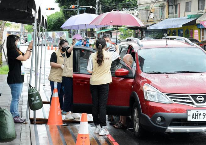 屏縣府社工為長輩撐傘，接送進入施打站。（林和生攝）