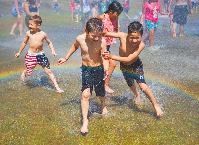 北美洲西北地區連日來遭遇熱浪侵襲。美國華盛頓州艾夫瑞特市消防隊利用消防灑水系統製造噴泉，供當地兒童玩水消暑。水花噴出時，還出現彩虹。（美聯社）