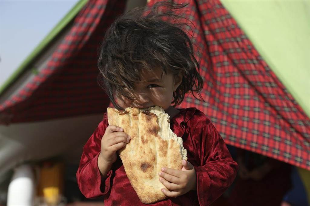 1名因流离失所的女孩，站在她临时搭建的帐篷前吃面包。(图/美联)(photo:ChinaTimes)