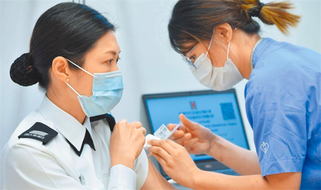 图为一名入境事务处人员（左）接种疫苗。（中新社）