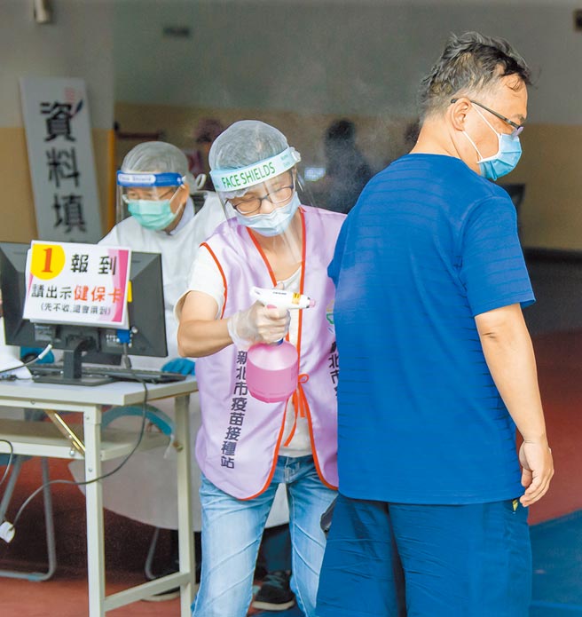 新庄综合体育馆17日疫苗接种相当踊跃，工作人员在民眾进场前帮忙全身喷酒精消毒。(罗永铭摄）